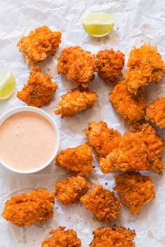 fried chicken nuggets with dipping sauce and limes next to it on a piece of parchment paper