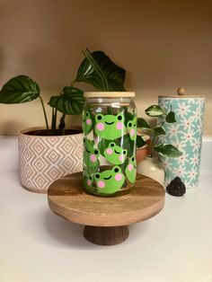 some plants are sitting on a table next to a jar with green and pink designs