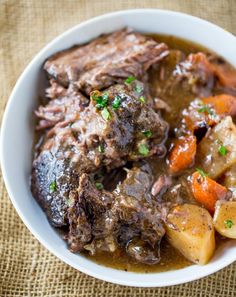 a white bowl filled with meat and vegetables on top of a brown cloth covered table