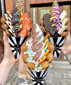 two people holding up ice cream cones with different toppings on them and one has chocolate, strawberries, candy, and marshmallows