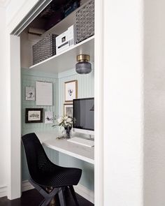 a desk with a computer on top of it in front of a white wall and black chair