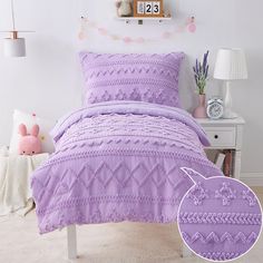 a bed with purple comforter and pillows in a room next to a white nightstand