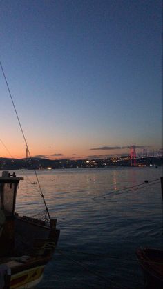 a boat sitting in the water at sunset with a bridge in the distance behind it