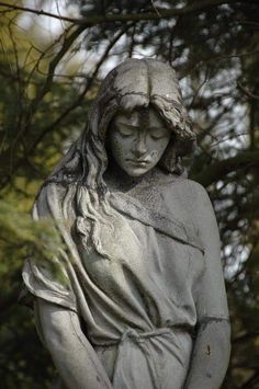 a statue of a woman with her hands in her pockets, standing next to some trees