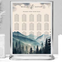 a wedding seating chart with mountains and pine trees in the background is displayed on a table