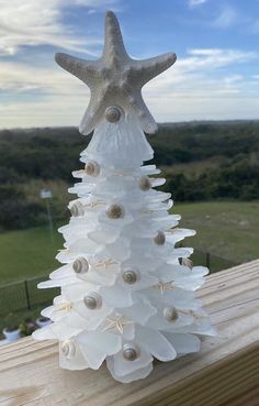 a white christmas tree made out of seashells and starfish shells on a wooden deck