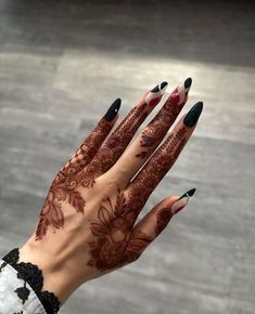 a woman's hand with henna on it and black nail polish, holding her hands out