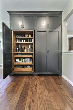 an open cabinet in the middle of a room with wood floors and white walls, is shown