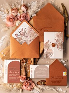 the wedding stationery is laid out on top of an envelope, with flowers and feathers