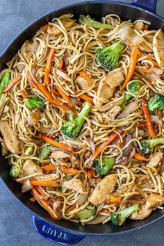 a skillet filled with noodles, broccoli and chicken