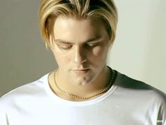 a man with blonde hair wearing a white t - shirt and gold chain around his neck