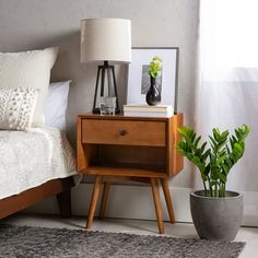 a bedroom with a bed, nightstand and plant in the corner on top of it