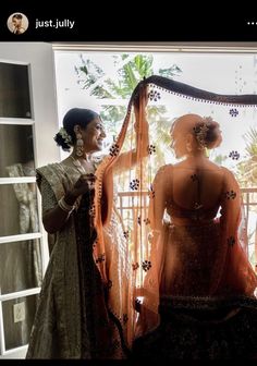 two women standing next to each other in front of a window with an orange curtain