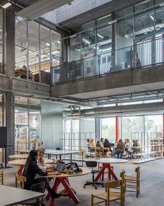 people are sitting at tables in the middle of an open area with lots of windows