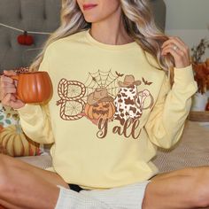 Boo Y'all cute Halloween Shirt. Witty and warm, you'll love this Western Halloween inspired crewneck!  Luxurious comfort and style are what this unisex, garment-dyed sweatshirt is all about. It's made with 80% ring-spun cotton and 20% polyester and the fabric is 3-end garment-dyed, ring-spun, color-blast fleece with a 100% cotton face. Each sweatshirt comes with a relaxed fit, a rolled-forward shoulder, and a back neck patch.  .: 80% ring-spun cotton, 20% polyester .: Medium-heavy fabric (9.5 oz Casual Fall T-shirt With Cow Print, Orange Crew Neck Halloween Sweatshirt, Halloween Graphic Print Crew Neck T-shirt, Spooky Orange Crew Neck T-shirt, Halloween Crew Neck T-shirt With Character Print, Ghost Shirt, Halloween Sweatshirt, Halloween Women, Halloween Shirt