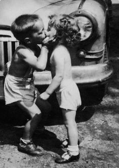 two young children standing next to an old car kissing each other's foreheads