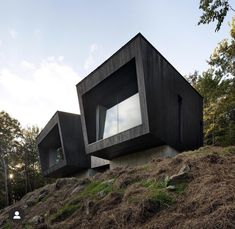 two black houses sitting on top of a hill next to grass and trees in the background