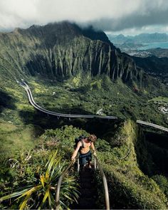 a man climbing up the side of a mountain with a view of a road and mountains in the background