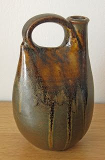 a brown and black vase sitting on top of a wooden table next to a white wall