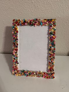 a small white frame with colorful beads on the edges and bottom, sitting on a table