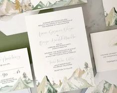 the wedding stationery is laid out on top of each other, with mountains in the background