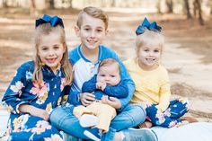 three children are sitting on a blanket in the woods and one is holding a baby