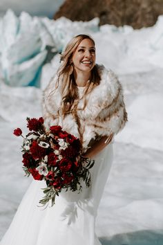 a woman in a white dress and fur stole holding a bouquet of flowers on her wedding day