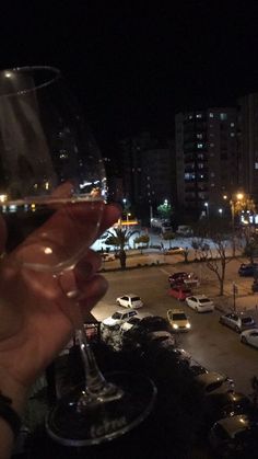 a person holding up a wine glass in front of a parking lot filled with cars