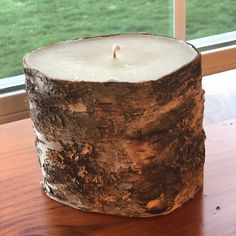 a close up of a candle on a table near a window with grass in the background