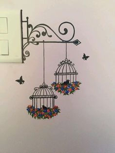 two birdcages with flowers and butterflies hanging from the side of a light switch