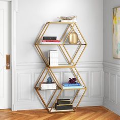 a gold shelving unit with books and magazines on it in a white walled room