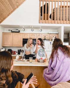 three women sitting at a kitchen counter talking to each other while one woman is holding a cell phone