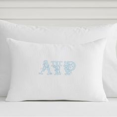 an embroidered pillow with the word gapa on it in light blue font, sitting on a white bed