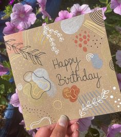 someone holding up a happy birthday card with flowers in the background