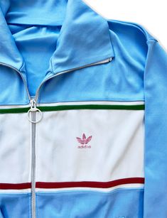 Adidas track jackets are highly sought after by collectors due to their unique design, limited availability, and historical significance. With iconic Adidas logo and stripes the retro graphics harken back to the style Farrah Fawcett wore on the tennis court and golf course. This one is rare due to it's gorgeous sky blue color and amazing collar. We love the red and green stripe accents; this jacket would go with anything! Also popularized by the hip-hop group, the Beastie Boys, in the 1980s. The Sporty Blue Track Jacket With Three Stripes, Retro Track Jacket With Three Stripes, Retro Streetwear Track Jacket With Three Stripes, Retro Track Jacket With Three Stripes For Streetwear, Retro Blue Track Jacket For Sports, Blue Retro Track Jacket For Sports, Retro Long Sleeve Track Jacket With Three Stripes, Vintage Three Stripes Track Jacket For Sports, Vintage Track Jacket With Three Stripes For Sports