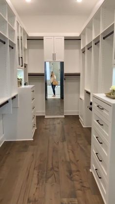 an empty walk in closet with white cabinets and drawers on both sides, while a woman is reflected in the mirror