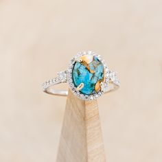 a ring with a blue stone surrounded by white and yellow diamonds on a wooden stand