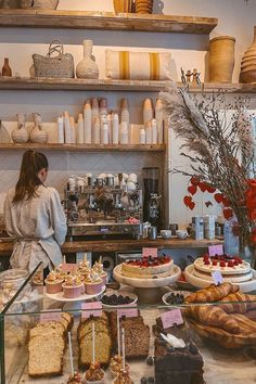 a woman standing in front of a counter filled with cakes and pastries