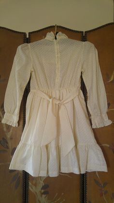 "70's Ivory and white polka dot print dress with hand smocked front and cream lace edging. Ties at sides. Long sleeves with frilly cuffs. High frilly collar. Zip up the back. Dress has underskirt Made by Polly Flinders Size 8 Hand smocked arm to arm across 14\" / bust 28, waist 23\", length 28\"" Vintage Cream Prairie Dress With Ruffles, Cream Vintage Dress With Ruffles For Spring, Fitted Retro Swiss Dot Dress, Retro Fitted Swiss Dot Dress, Spring Cream Prairie Dress For Daywear, Cream Prairie Dress With Ruffles In Cottagecore Style, Retro Swiss Dot Dress, Cream Cottagecore Prairie Dress With Ruffles, Cream Prairie Dress With Lace Trim For Spring