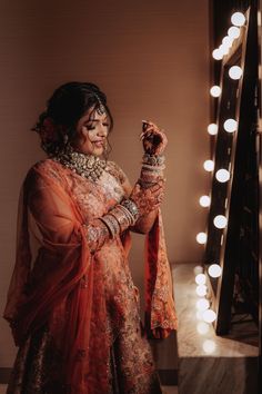 a woman is standing in front of a mirror with lights on the wall behind her