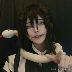 a woman with black hair and blue eyes is holding a snake in her hand while wearing a striped shirt