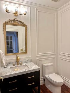 a white toilet sitting next to a sink in a bathroom under a golden framed mirror