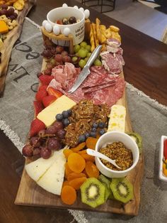 an assortment of cheeses, meats and fruits on a wooden platter with bowls of fruit