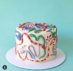 a white cake with colorful icing on top of a blue table next to a green wall