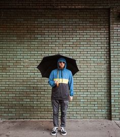 a man standing in front of a brick wall with an umbrella over his head,