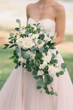 a woman in a wedding dress holding a bridal bouquet with white flowers and greenery