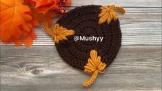 a crocheted hat with leaves on it sitting next to an orange and yellow flower