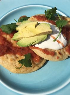 two tortillas on a blue plate topped with avocado and sour cream