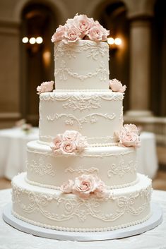 a three tiered wedding cake with pink flowers on the top and bottom, sitting on a white table cloth