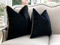 two black pillows sitting on top of a white couch next to a potted plant